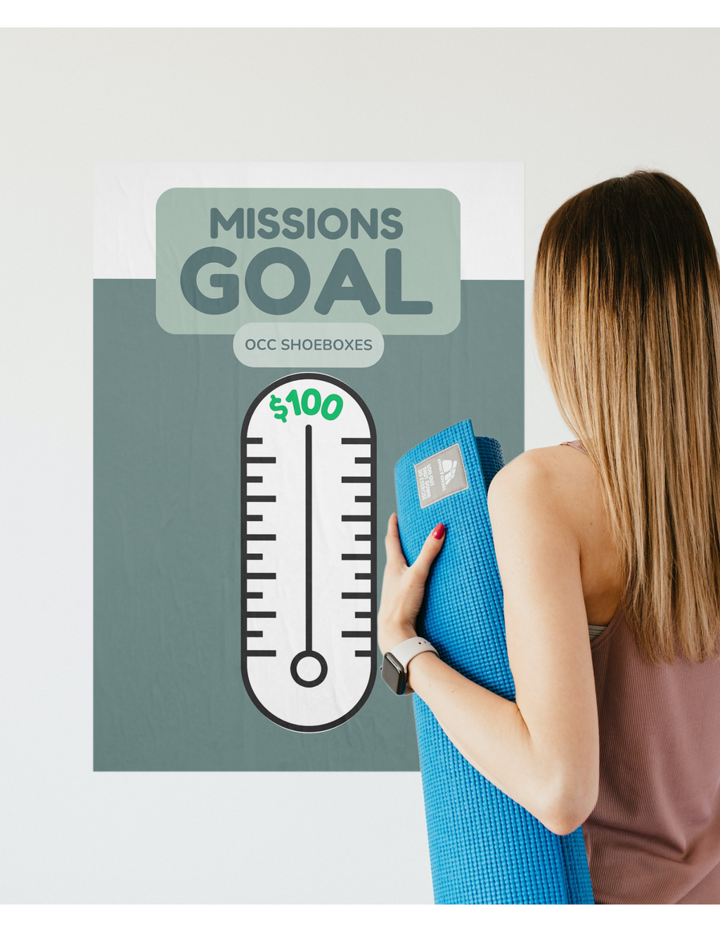 Woman holding a blue yoga mat in front of a 'Missions Goal' thermometer poster.